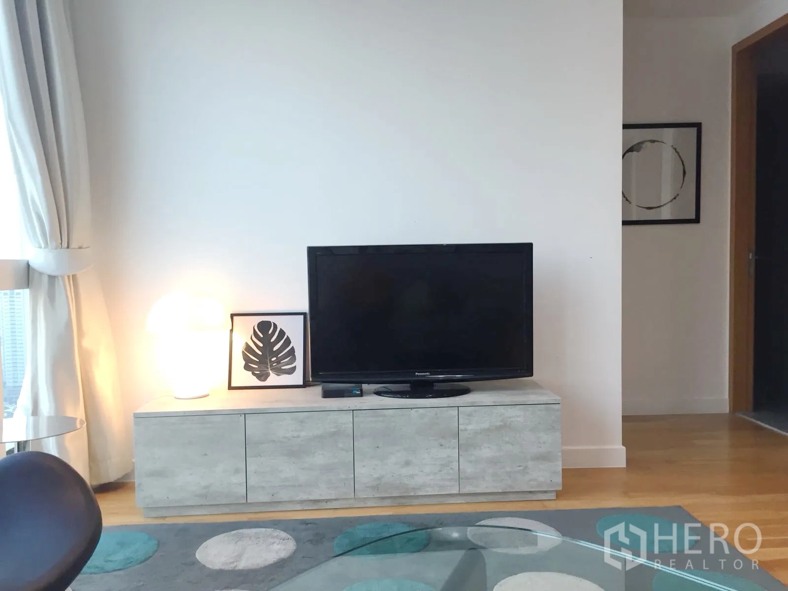 Condominium for rent or sale in Khlong Toei, Bangkok - TV console with flat-screen, soft lamp lighting and city-view windows in the living room.
