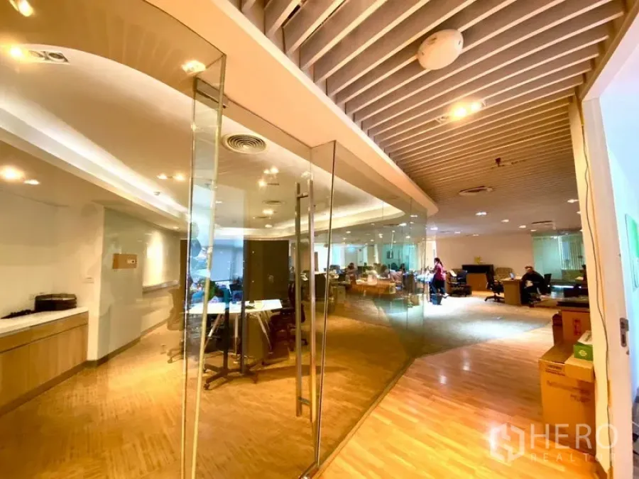 Office Space for rent in Watthana, Bangkok - Open-plan office with glass-partitioned meeting room, wooden floors, built-in cabinetry, and bright overhead lighting.