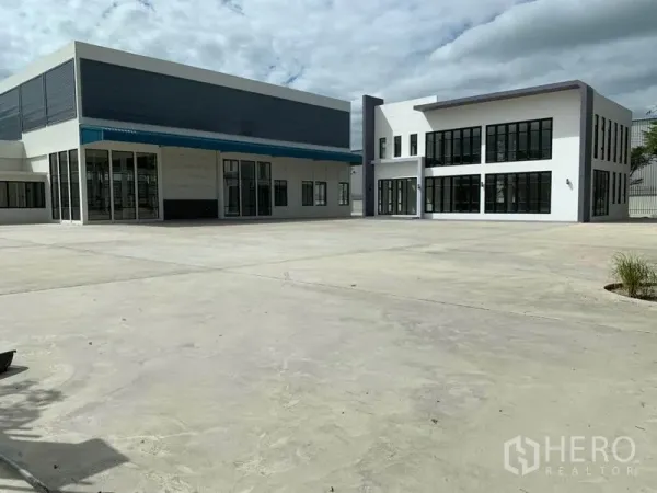 Warehouse for rent in Bang Phli, Samut Prakan - Spacious concrete yard in front of a warehouse with a canopy and a glass-front office building.