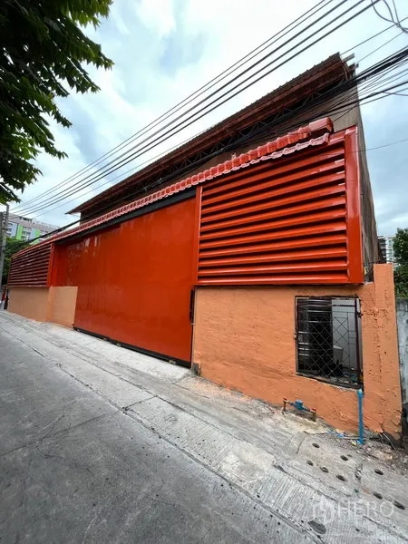 Warehouse for rent in Din Daeng, Bangkok - Street-facing orange warehouse facade with long metal sliding doors and roof canopy.