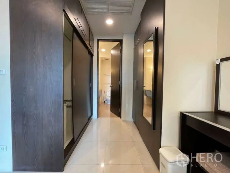 Apartment for rent in Khlong Toei, Bangkok - Hallway with sliding-door wardrobes leading toward the bathroom.