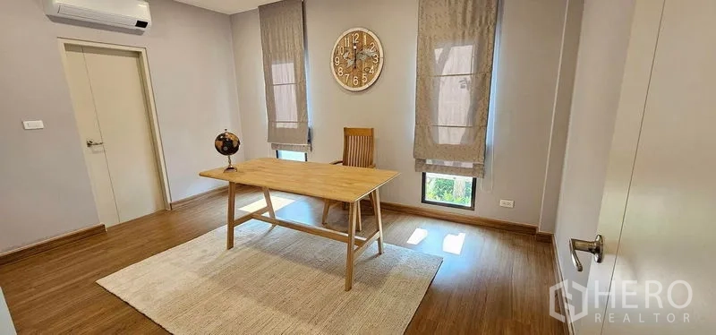 Detached House for rent in Bang Phli, Samut Prakan - Minimalist home office with wooden desk, wall clock and tall windows.