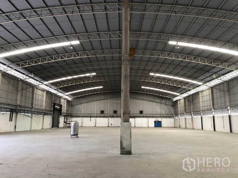 Factory for rent in Phra Nakhon Si Ayutthaya - Open factory floor with central columns beneath a curved metal truss roof and bright strip lighting.
