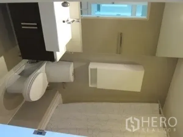 Condominium for rent in Khlong Toei, Bangkok - Modern bathroom with vanity, toilet and a window bringing in natural light.