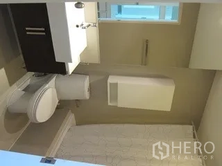 Condominium for rent in Khlong Toei, Bangkok - Modern bathroom with vanity, toilet and a window bringing in natural light.