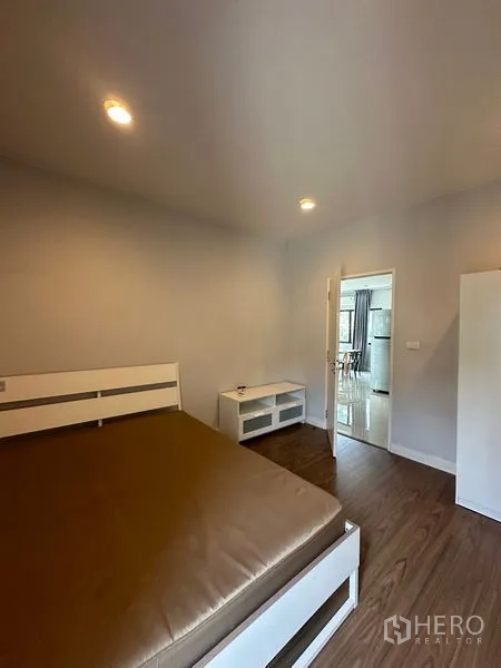 Detached House for rent in Lam Luk Ka, Pathum Thani - Cozy bedroom with wood flooring, bed frame and TV console.