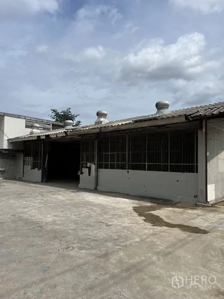 Warehouse for rent in Bangkok - Single-storey warehouse exterior with turbine roof vents and wide concrete yard.