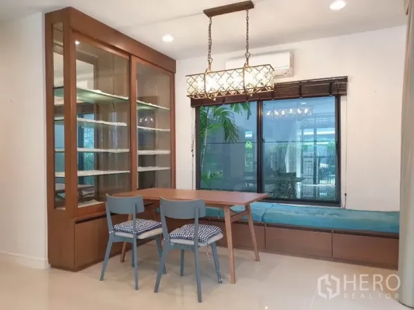 Detached House for rent in Bang Kapi, Bangkok - Dining nook featuring a wooden table, bench seating by the window, pendant lights, and a built-in glass display cabinet.