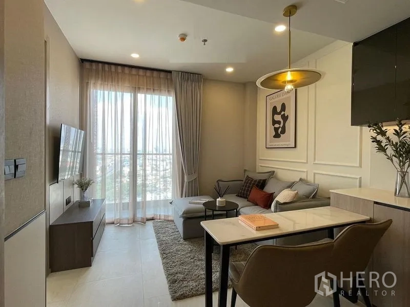 Condominium for rent in Pathum Wan, Bangkok - Living room with balcony-style window, L-shaped sofa and TV opposite.