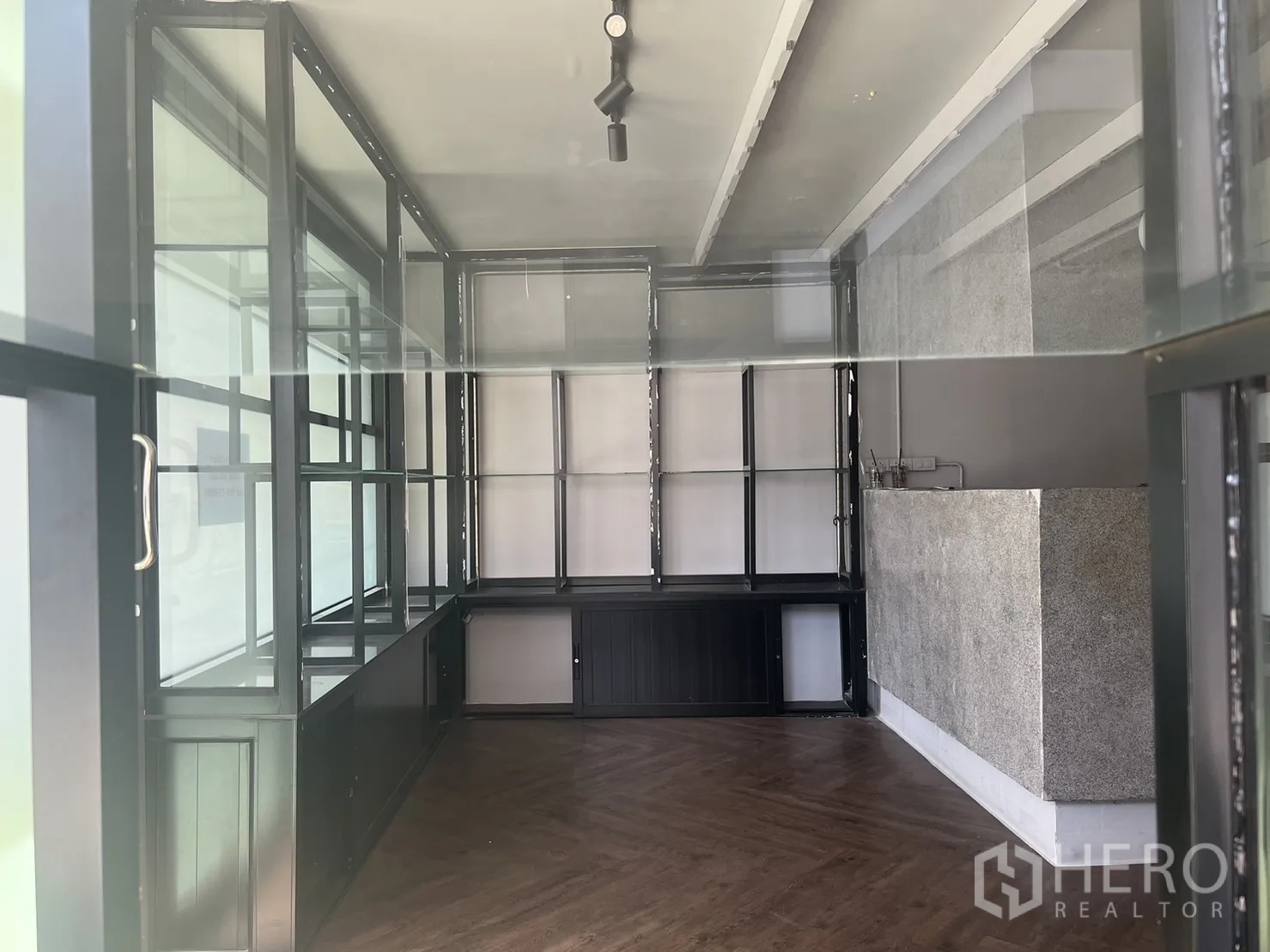 Retail Space for rent in Watthana, Bangkok - View through the window into the retail interior with glass shelving, a stone counter and herringbone floor.