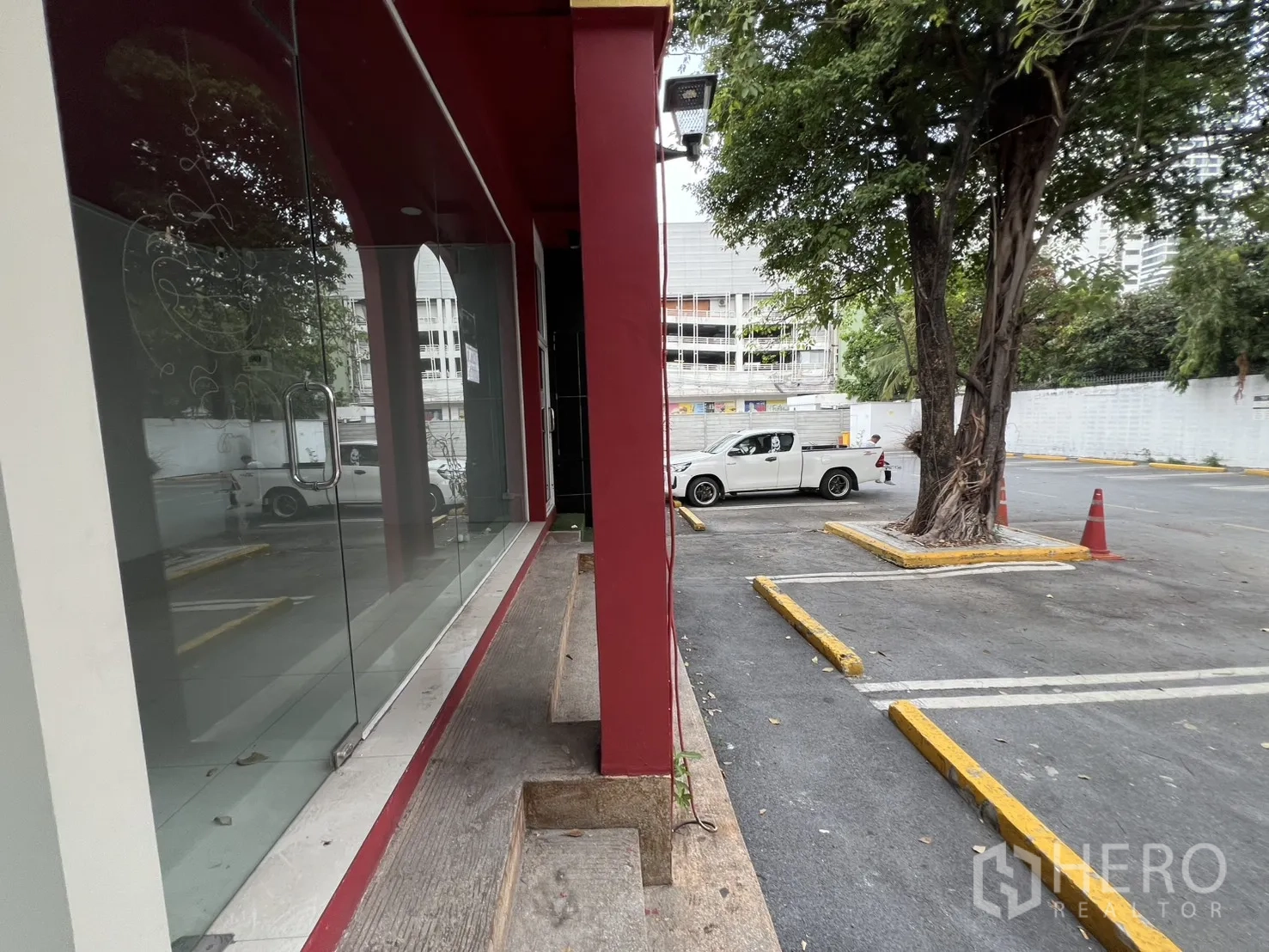 Retail Space for rent in Watthana, Bangkok - Side walkway beside full-height display windows leading to an open parking lot with a large shade tree.