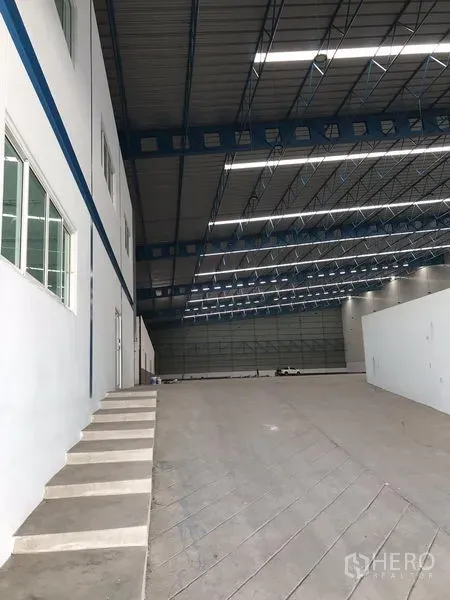 Warehouse for rent in Samut Prakan - Internal office block with windows beside a loading ramp under a high-bay roof inside the warehouse.