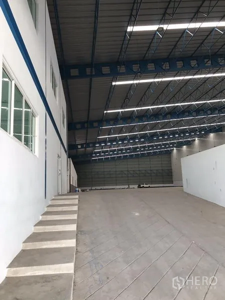 Warehouse for rent in Samut Prakan - Internal office block with windows beside a loading ramp under a high-bay roof inside the warehouse.