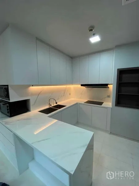 Condominium for rent or sale in Khlong Toei, Bangkok - Modern U-shaped white kitchen with marble countertops, under-cabinet lighting and ample storage.
