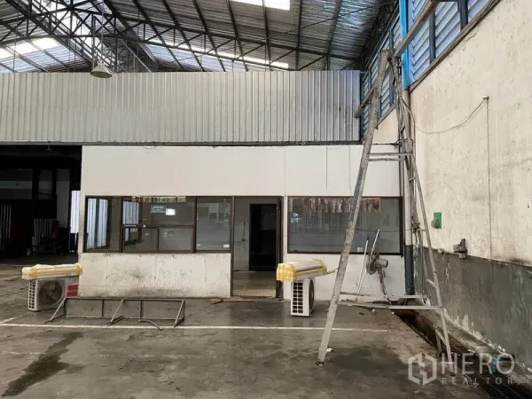 Warehouse for rent in Prawet, Bangkok - Warehouse interior with partitioned office cabin, steel truss roof, and polished concrete floor.