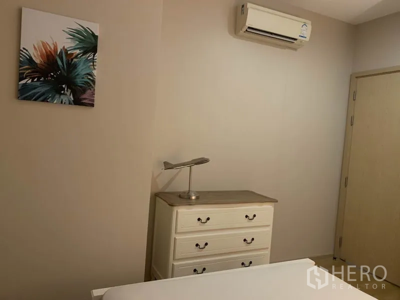 Condominium for rent in Watthana, Bangkok - Second bedroom corner with white dresser, wall art, air conditioner and wooden door.