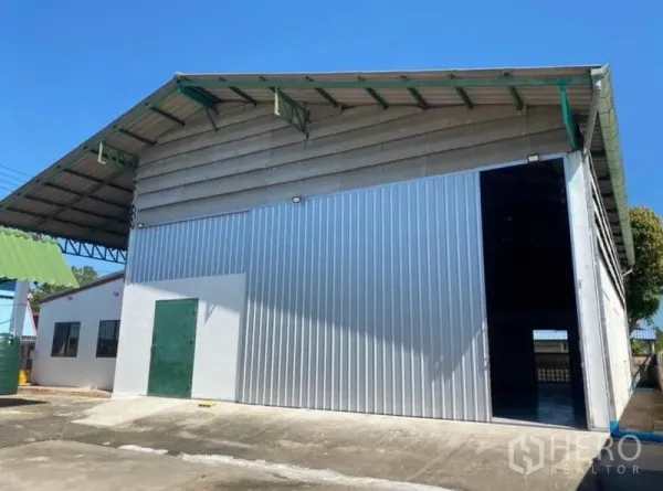 Warehouse for rent in Mueang Rayong, Rayong - Front facade of a high-clearance metal warehouse with a large sliding door and side service room.
