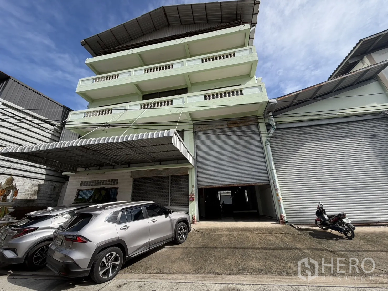 Factory for rent or sale in Bang Bon, Bangkok - Multi-story factory facade with roller shutters and a parking area.