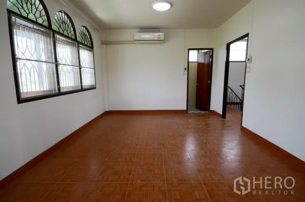Home Office for rent in Lat Phrao, Bangkok - Bright upstairs room with arched windows, security grilles, air‑conditioner and tile floors.
