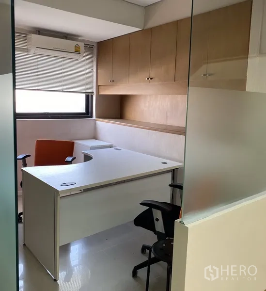 Office Space for rent in Din Daeng, Bangkok - Private office with white L-shaped desk, window blinds and overhead wooden cabinets behind a glass partition.