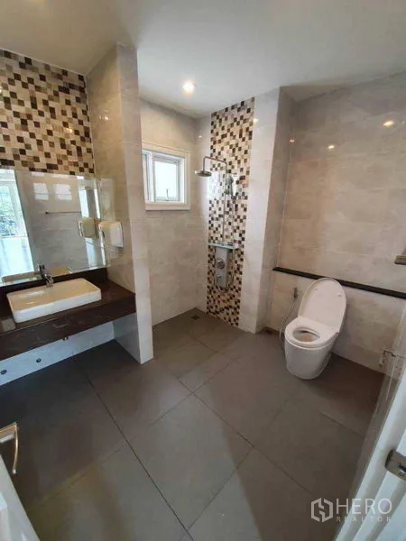 Townhouse for rent in Bang Na, Bangkok - Bathroom with mosaic accent tiles, rain shower, vanity with mirror and gray floor tiles.