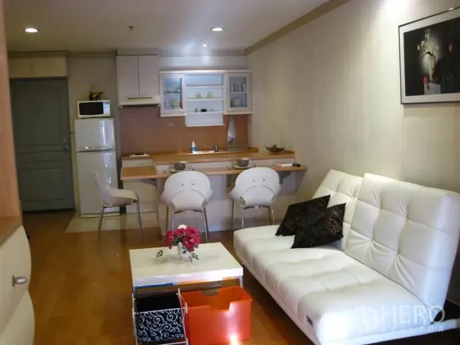 Condominium for rent in Khlong Toei, Bangkok - Open-plan living area with white sofa, wood floors, and compact kitchen with breakfast bar and stools.