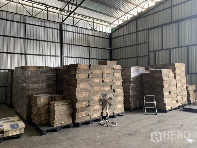 Warehouse for rent in Bang Kapi, Bangkok - Large storage area with high metal walls and tall stacks of cardboard on pallets.