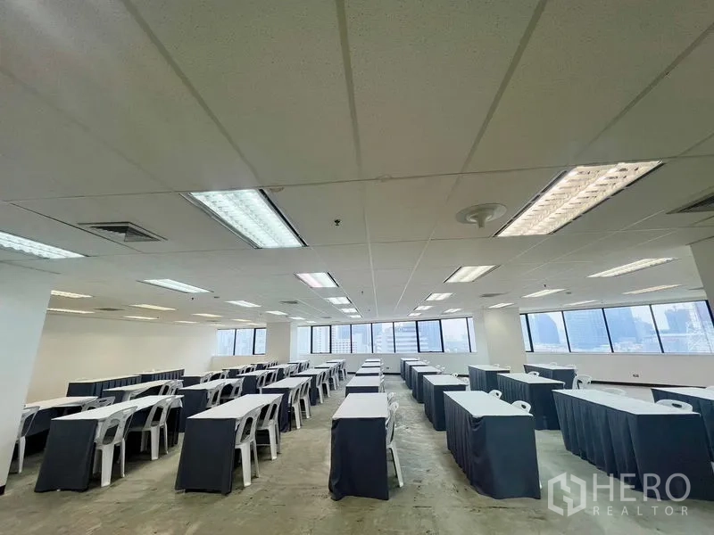 Office Space for rent - Classroom-style layout under grid ceiling with fluorescent lighting and wide windows across the wall.