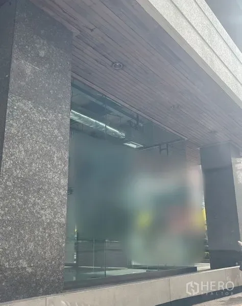 Retail Space for rent - Close-up of glass storefront beneath stone pillars and a timber ceiling soffit.