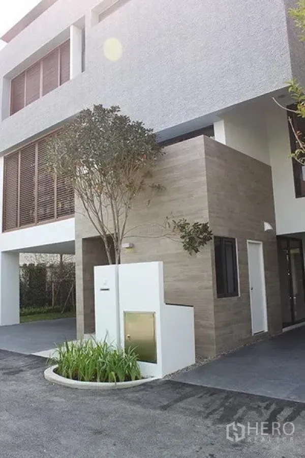 Detached House for rent in Huai Khwang, Bangkok - Modern three-storey detached house exterior with carport, wood-and-concrete facade and a landscaped entry.