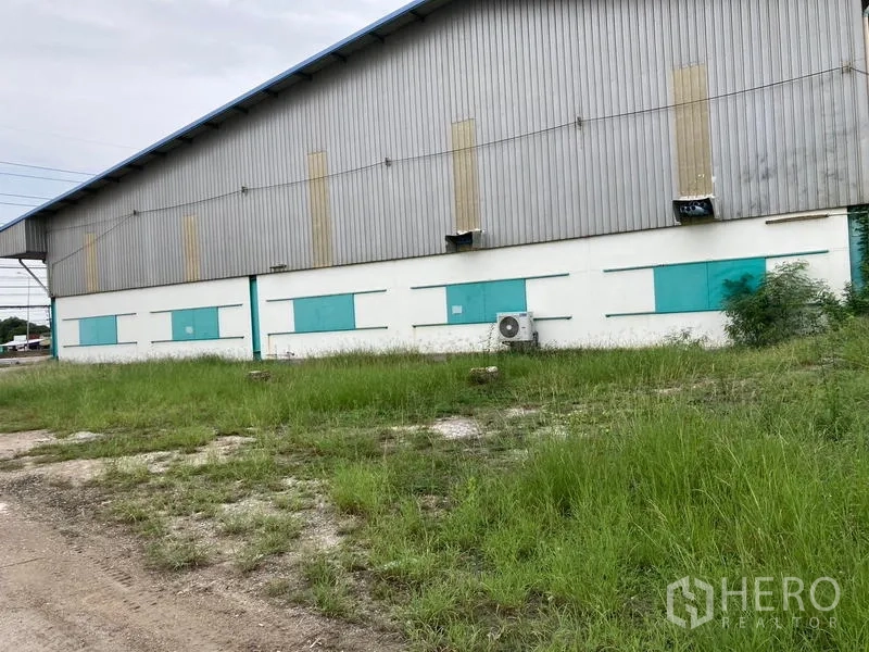 Warehouse for rent in Mueang Samut Sakhon, Samut Sakhon - Rear exterior wall of the warehouse with ventilation panels and grassy verge.