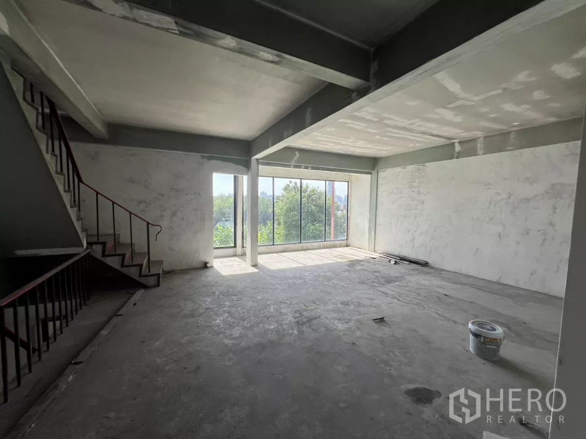 Shophouse for sale in Suan Luang, Bangkok - Open-plan upper floor with floor-to-ceiling windows and a steel staircase in a semi-renovated shophouse.