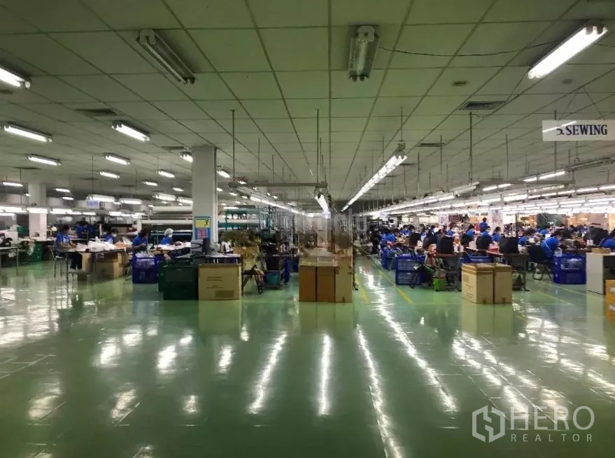 Factory for sale in Khlong Luang, Pathum Thani - Large production hall with bright fluorescent lighting, polished floor and organized workstations and equipment.