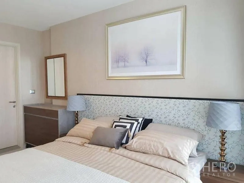 Condominium for rent or sale in Khlong Toei, Bangkok - Calm bedroom with upholstered headboard, bedside lamps, dresser and framed artwork.