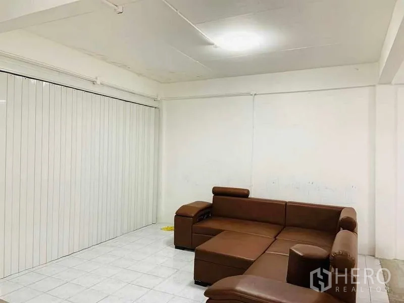 Shophouse for rent or sale in Khlong Toei, Bangkok - Private room with brown L-shaped leather sofa, white tile floor and a sliding partition wall.