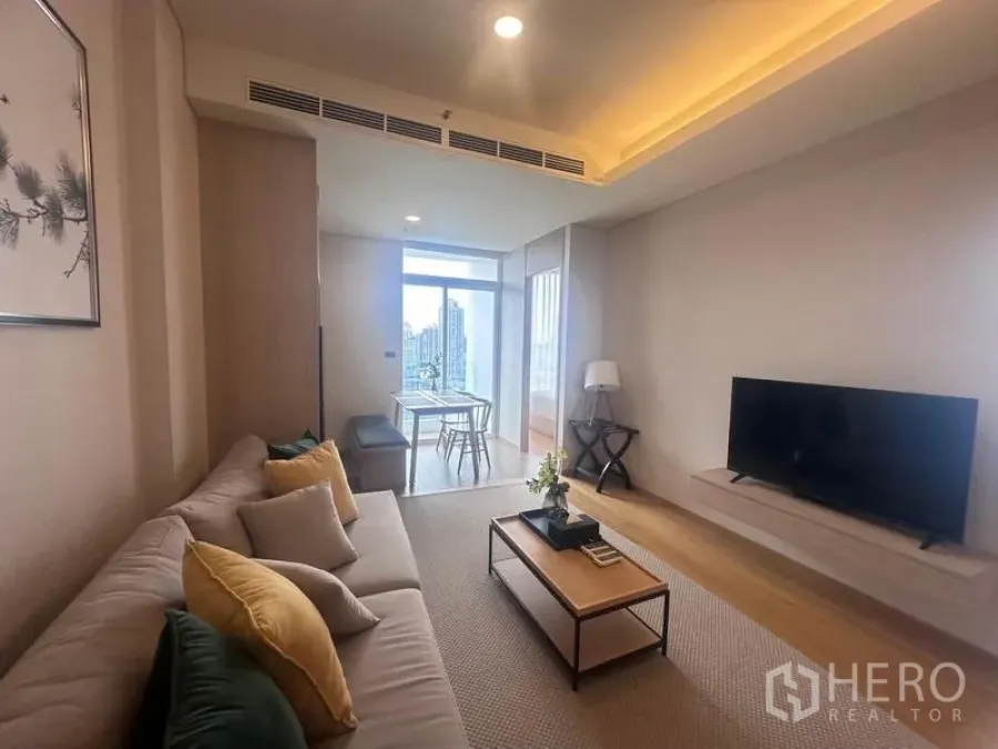 Condominium for rent - Warm-toned living room with sectional sofa, coffee table, wall-mounted TV and dining nook by a large window with city view.