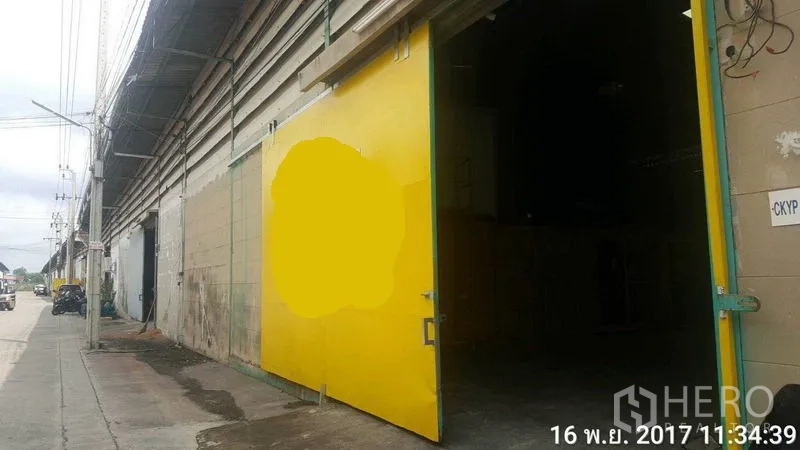 Factory for rent in Bang Phli, Samut Prakan - Open yellow metal gate showing the factory entrance and driveway.