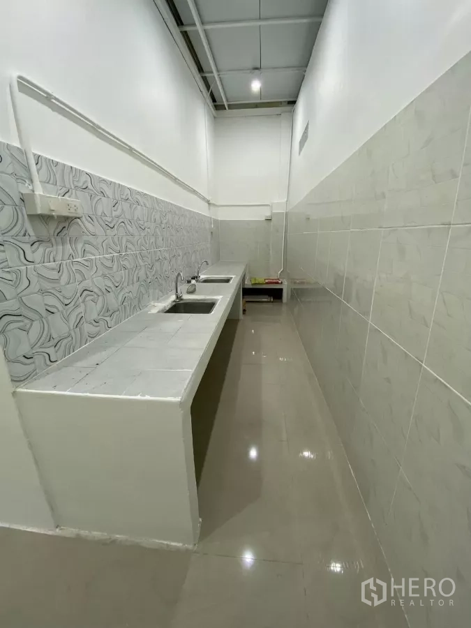 独立式住宅 出租在Bang Na, Bangkok - 窄长式泰式湿厨，瓷砖台面，双不锈钢水槽与高挑顶。