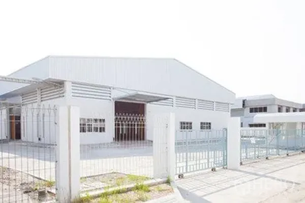 Factory for rent in Chachoengsao - Front view of a white warehouse behind a steel fence and sliding entrance gate.