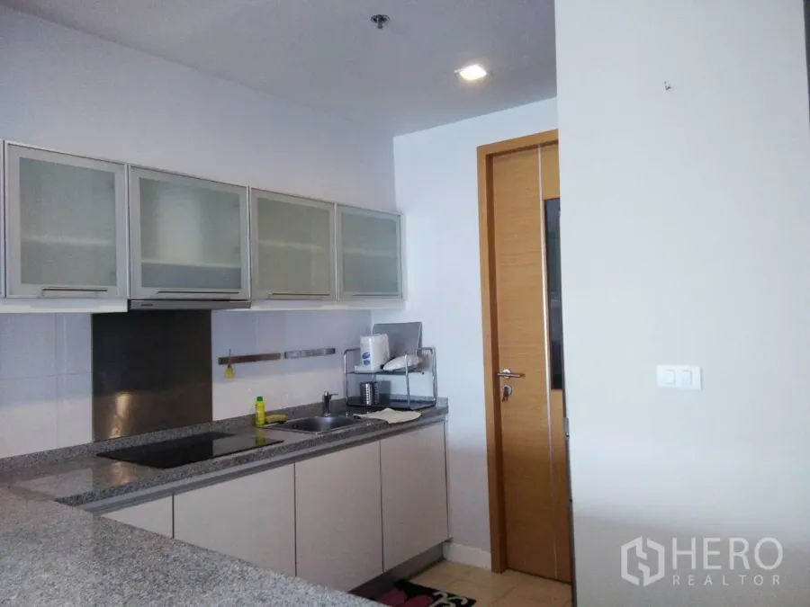 Condominium for rent in Khlong Toei, Bangkok - Modern condo kitchen with granite countertops, induction cooktop, and frosted-glass cabinets.