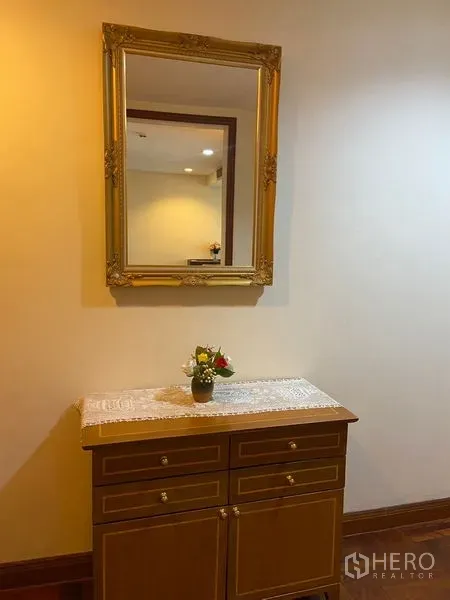 Condominium for rent in Pathum Wan, Bangkok - Console cabinet with an ornate gold-framed mirror and a small flower vase under warm lighting.
