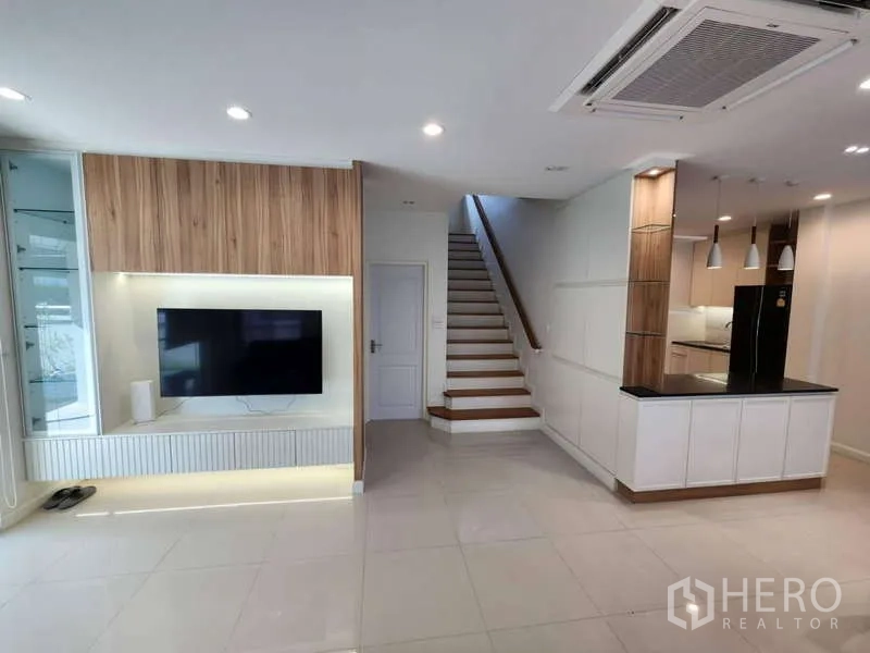 Detached House for rent in Sathon, Bangkok - Bright living room showing media wall, staircase, and kitchen island.