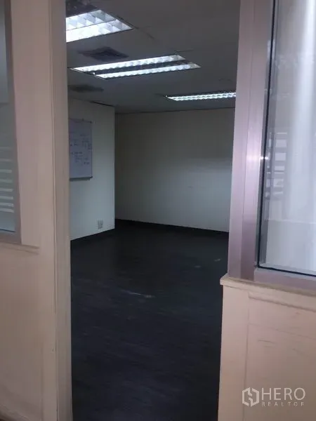 Office Space for rent in Watthana, Bangkok - Entry to a small office through glass partition with dark flooring and ceiling lights.