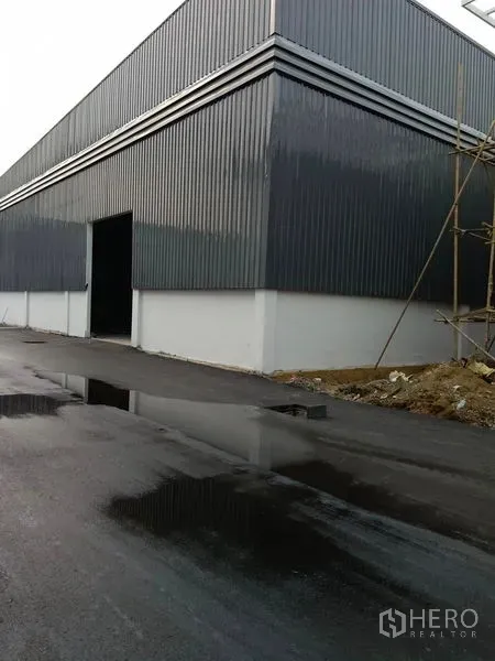 Warehouse for rent in Khlong Toei, Bangkok - Corner view of a warehouse with an open loading door beside a wet asphalt access road.