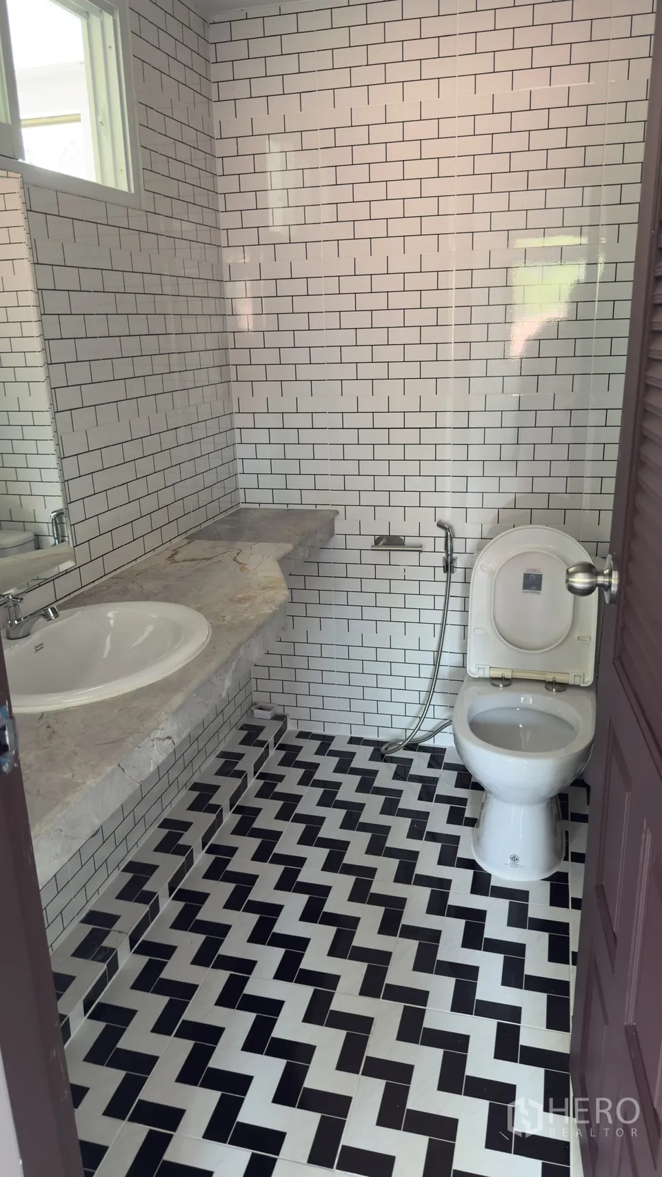 Townhouse for rent in Watthana, Bangkok - Compact bathroom with white subway tiles, patterned black-and-white floor, stone counter, and toilet with bidet spray.