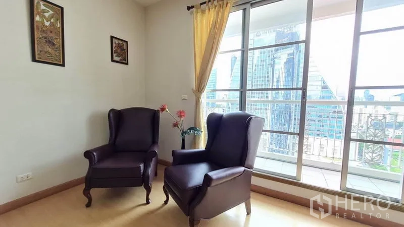 Condominium for rent in Khlong Toei, Bangkok - Cozy corner seating with two armchairs beside sliding glass doors to a balcony and skyline panorama.