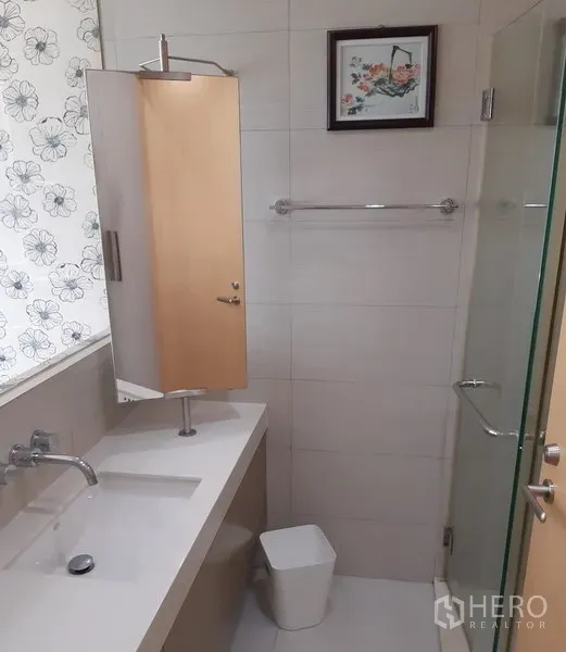 Condominium for rent in Khlong Toei, Bangkok - Clean bathroom with long vanity, large mirror, glass-enclosed shower and patterned blind.