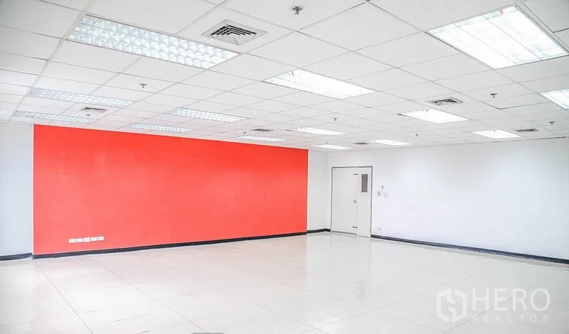 Office Space for rent in Bang Na, Bangkok - Large office room facing a red accent wall under fluorescent lighting.