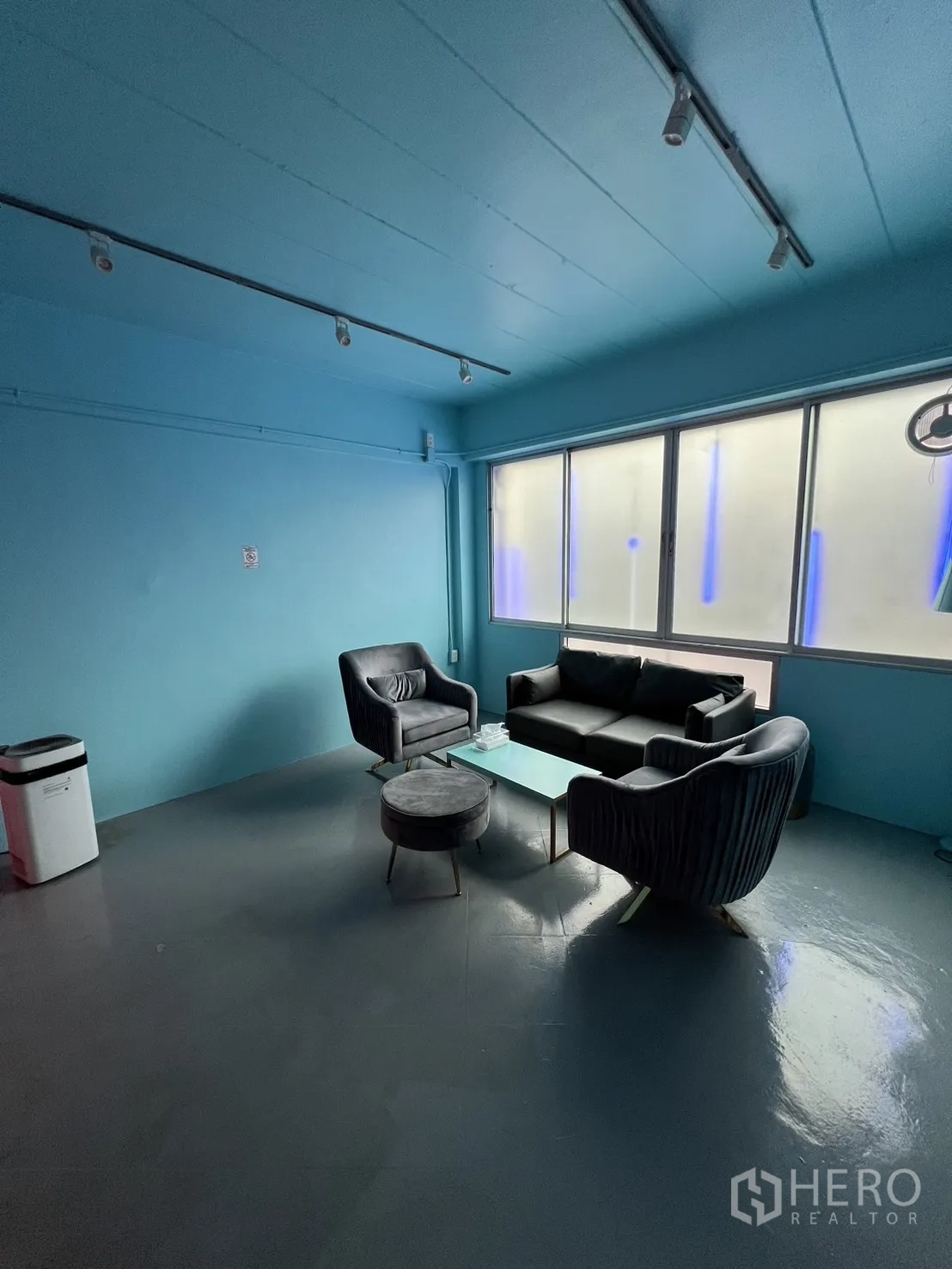 Shophouse for rent or sale in Watthana, Bangkok - Spacious blue room with sofa set and track lighting overlooking frosted windows.