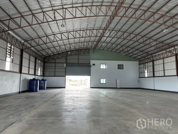 Factory for rent or sale in Sai Noi, Nonthaburi - Spacious warehouse interior with high arched steel truss roof, polished concrete floor and roller shutter door.